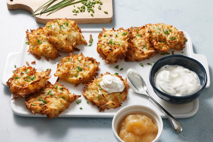 High-angle view of golden, crispy air-fryer latkes on a plate, accompanied by small bowls of sour cream and applesauce.
