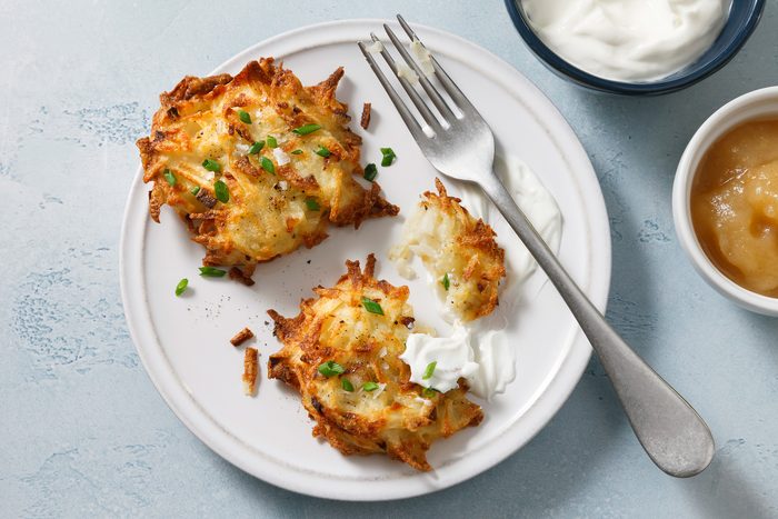 Overhead view of crispy air-fryer latkes on a plate, served with a side of sour cream and applesauce.