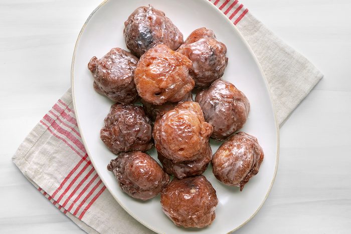 overhead shot of a white plate filled with a dozen of Apple Fritters; the plate is sitting on a white marble surface with a white linen napkin with red stripes beside it
