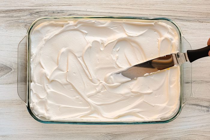 Spreading the whipped topping over the pudding layer.