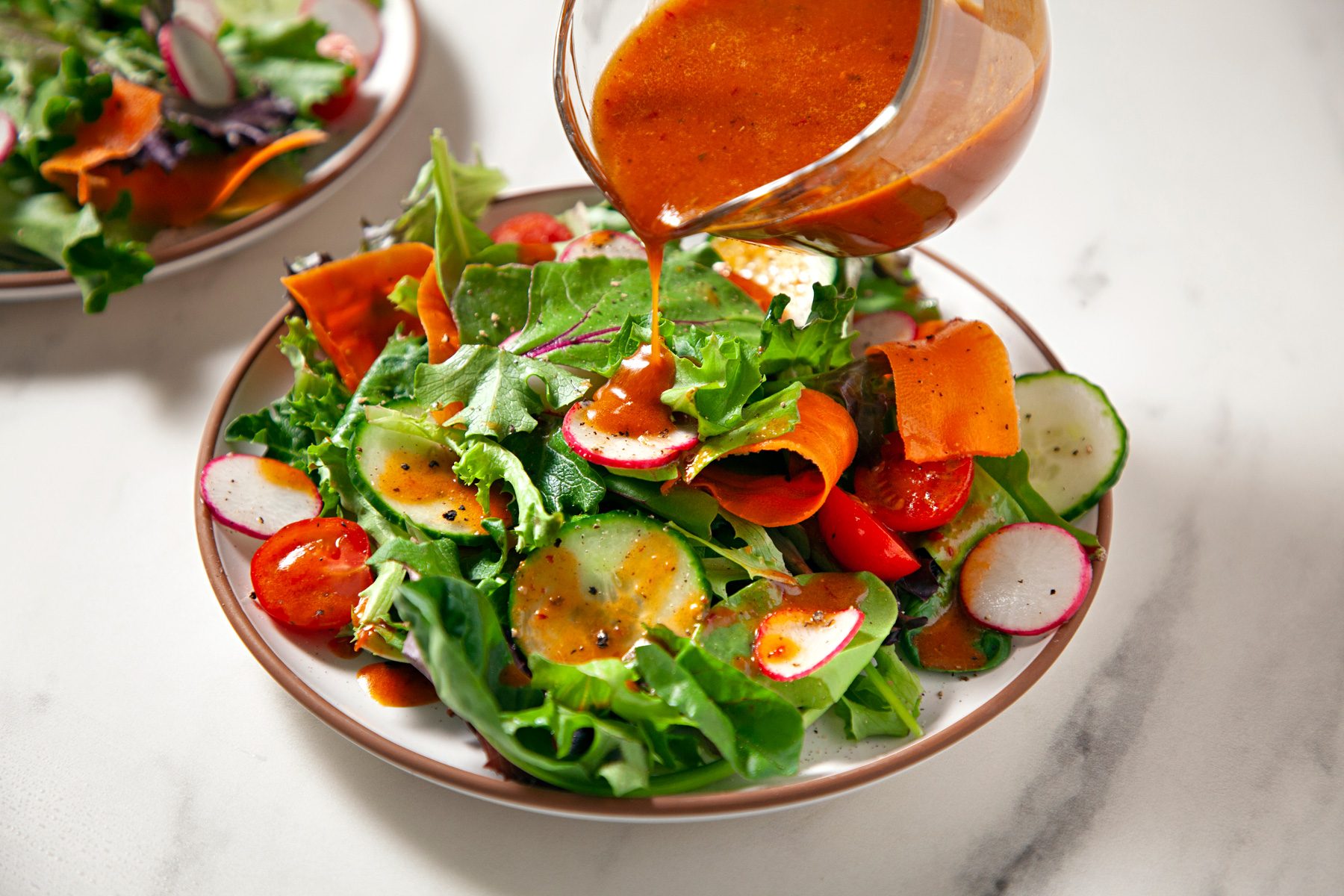 Chipotle honey vinaigrette dressing being drizzled over a bowl of fresh salad.