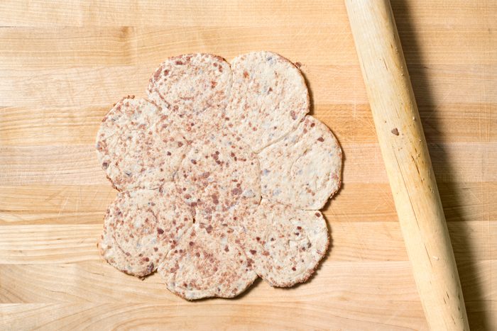overhead shot of a wooden cutting board with a rolling pin laying on the right side of the image; a circle of dough is placed in the center of the cutting board; the dough is cut into eight slices with a brown filling