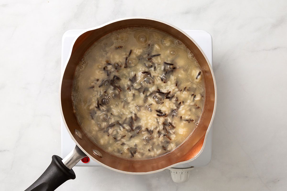 Wild rice and long grain rice boiling in water and chicken bouillon mixture in a saucepan for step one of Cornish Game Hens with Wild Rice Stuffing recipe for Taste of Home