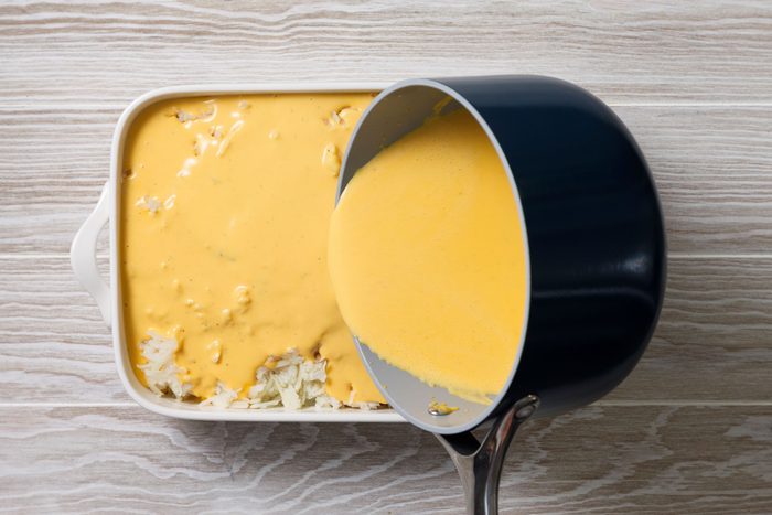 Pouring of cheese sauce on shredded potatoes
