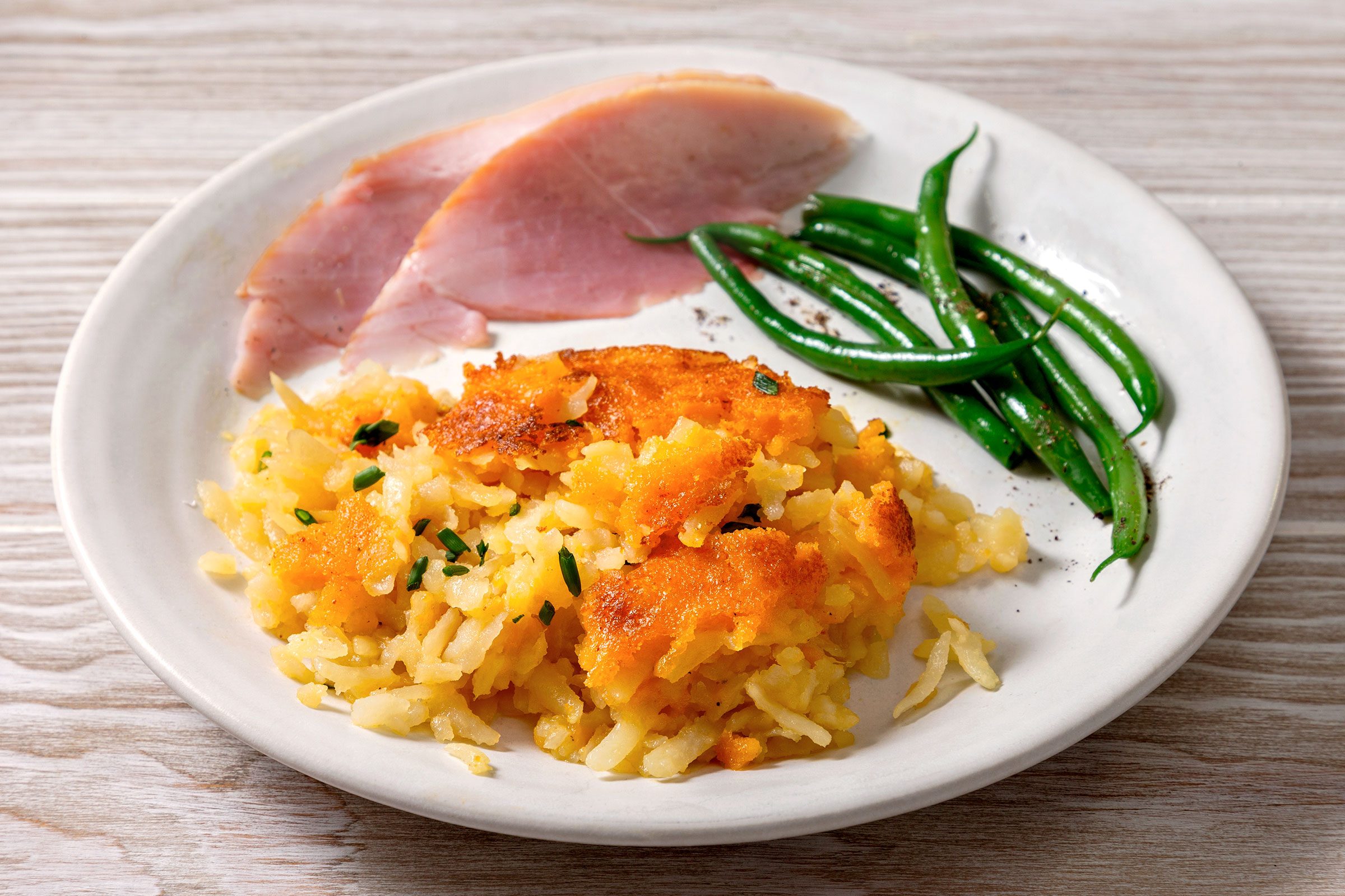 Delmonico Potatoes served in a plate with some meat and greens on side