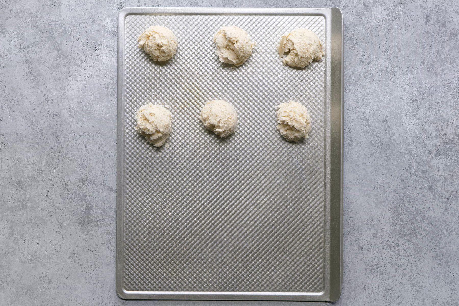 Overhead shot of drop by 1/4 cupfuls 1 inch apart onto greased baking sheets; bake until bottoms are golden brown; 17-20 minutes; Serve warm; grey surface;