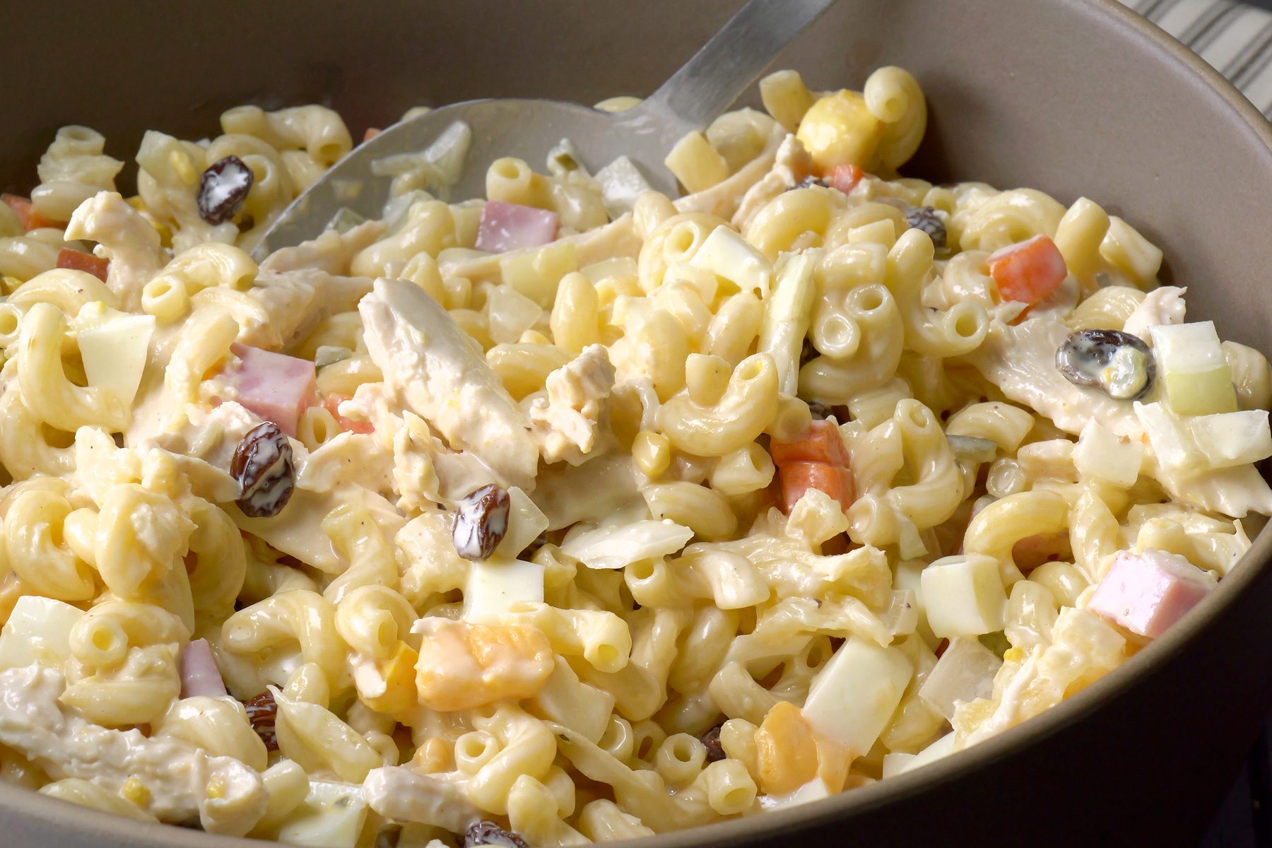close shot of a bowl of macaroni salad with a fork in it; the salad is sitting on a brown and white striped napkin;