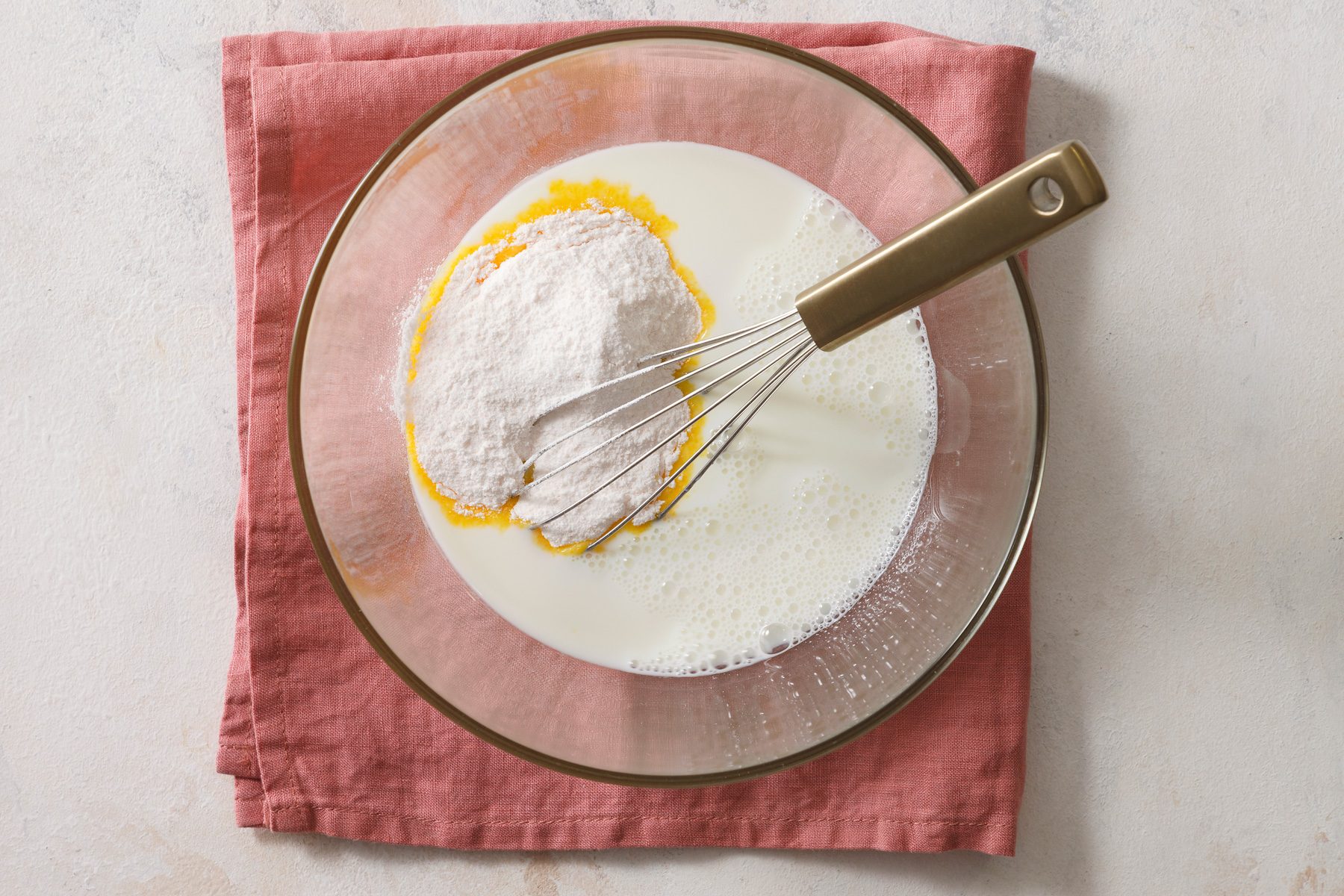 Overhead shot of a large bowl whisk milk and pudding mix for 2 minutes; let stand for 2 minutes or until soft-set; whisk tool; napkin; marble surface.