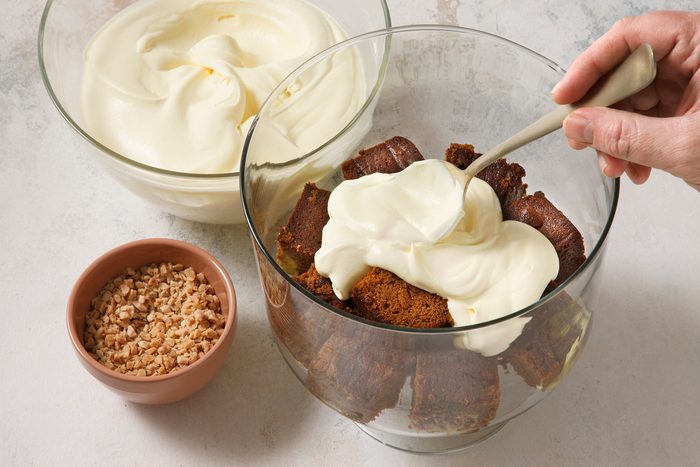 High angle view shot of a serving bowl; layer half of the cake cubes and half of the pudding mixture; sprinkle with 1/2 cup toffee bits; spoon; marble surface.