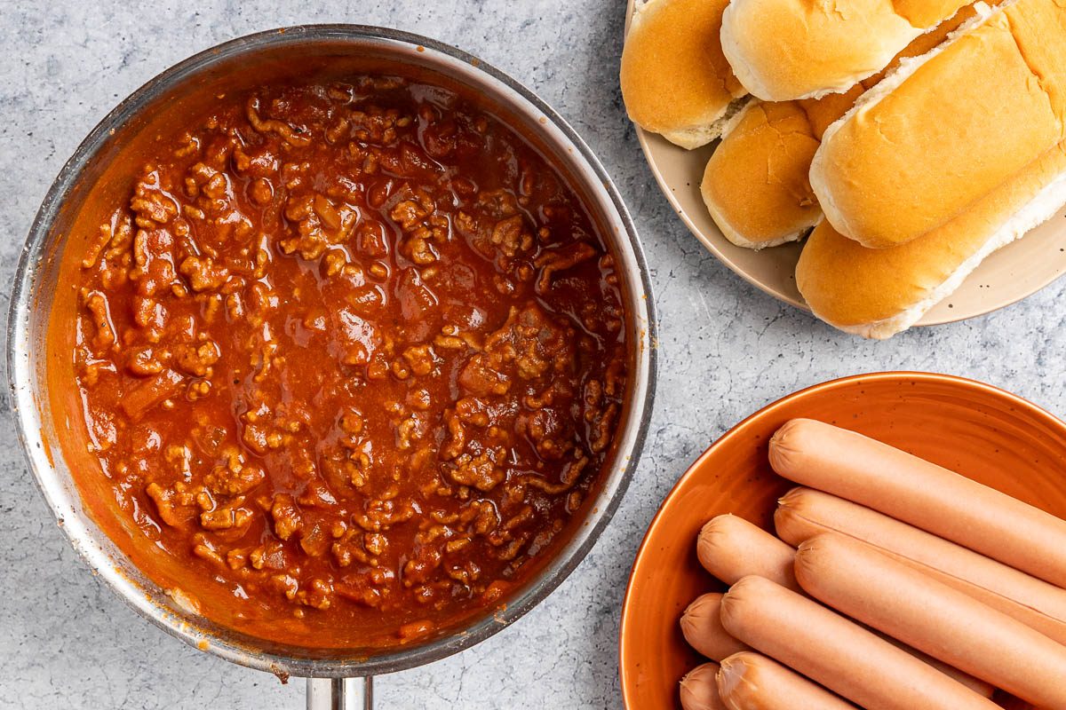 Taste of Home Hot Dog Sauce photo of all the ingredients heated in a saucepan with hot dogs and buns peeking into frame.