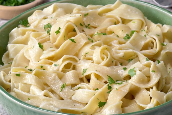 Egg noodles sprinkled with parsley served in a green bowl