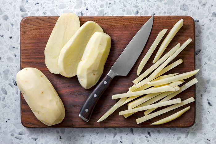 Potatoes cut into thin strips with a big knife on a wooden chopping board