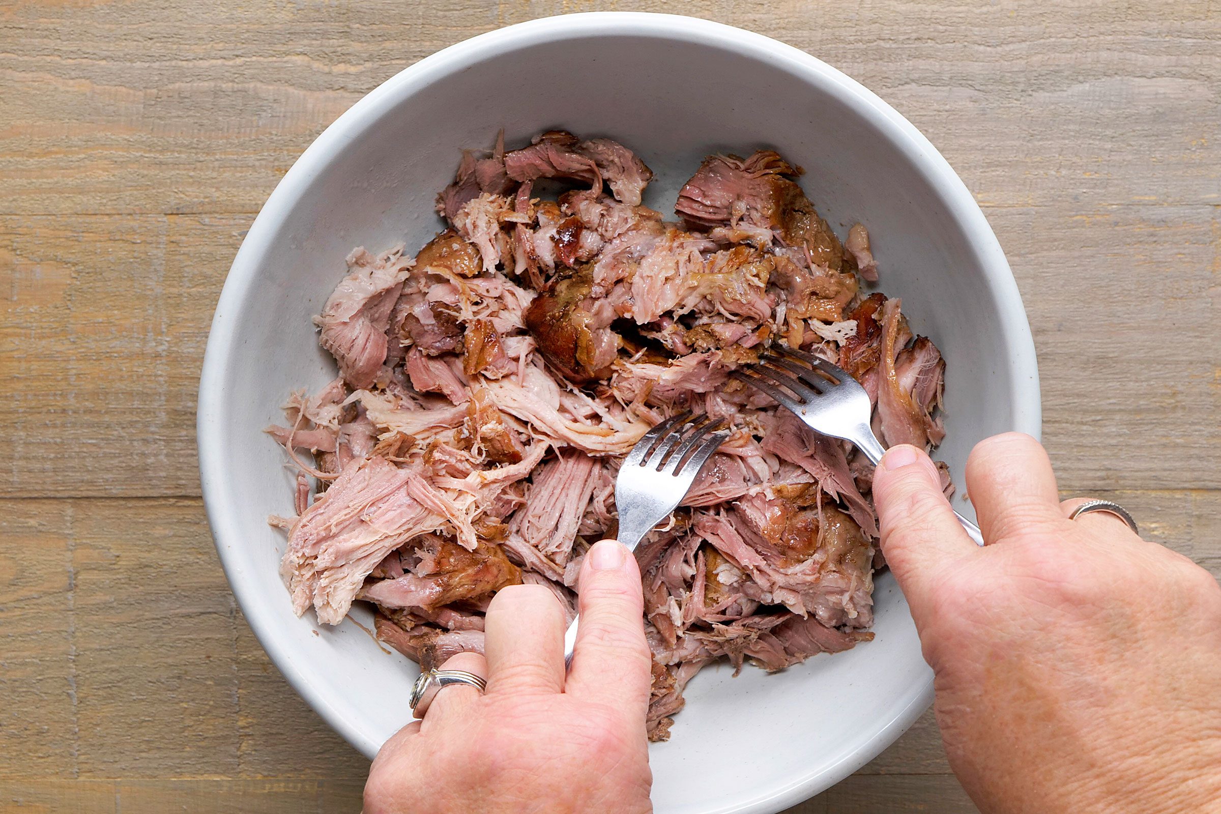 Shredding pork meat with a fork in a bowl