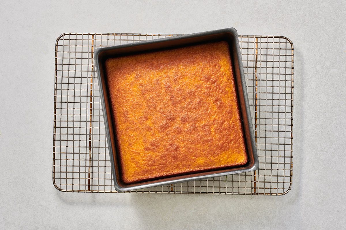 Baked cake in a square baking pan, golden brown and evenly cooked, cooling on a rack.
