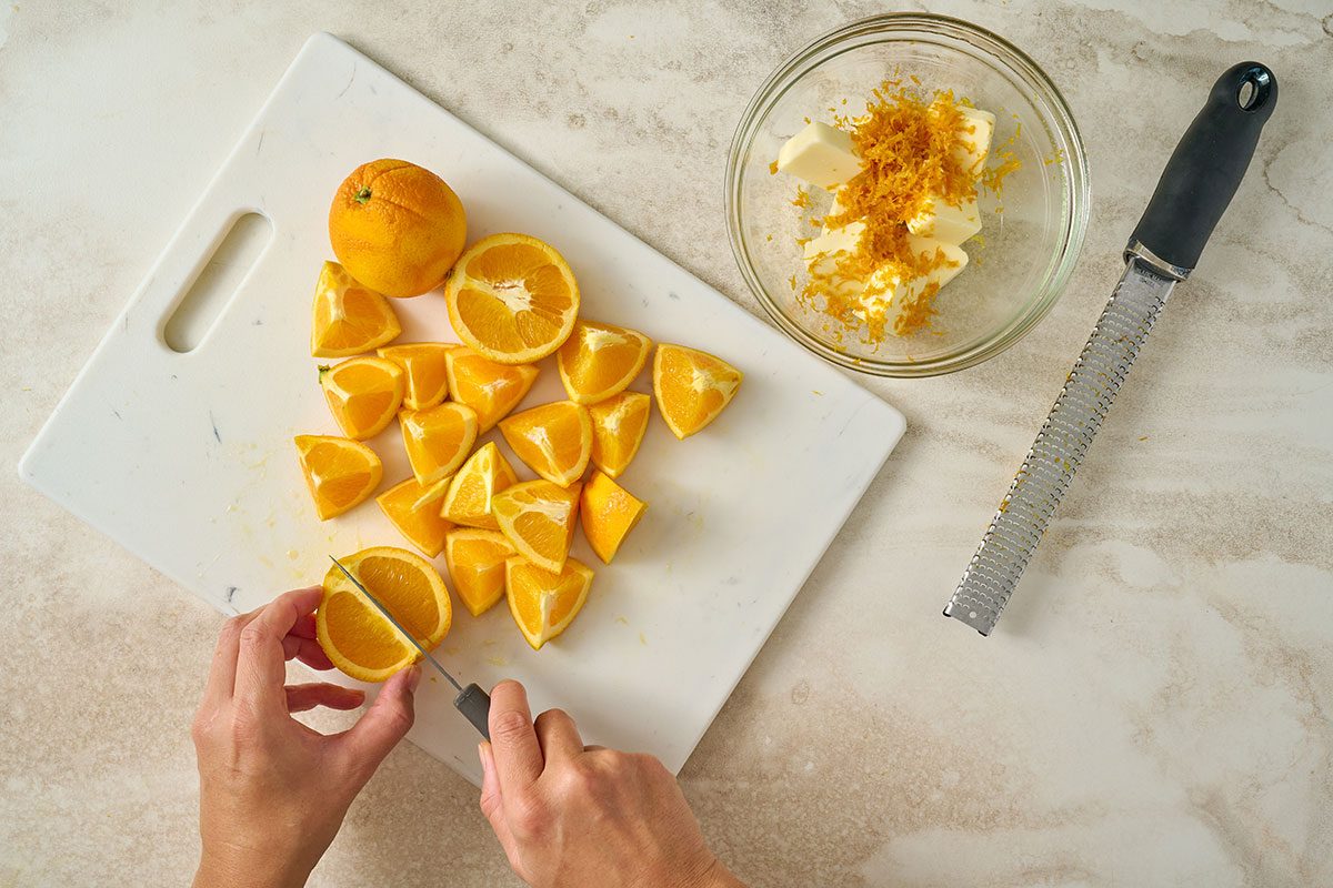 Overhead view of orange being sliced into wedges and zest being combined with softened butter in preparation for seasoning beneath the turkey skin for the Taste of Home Orange Turkey recipe.