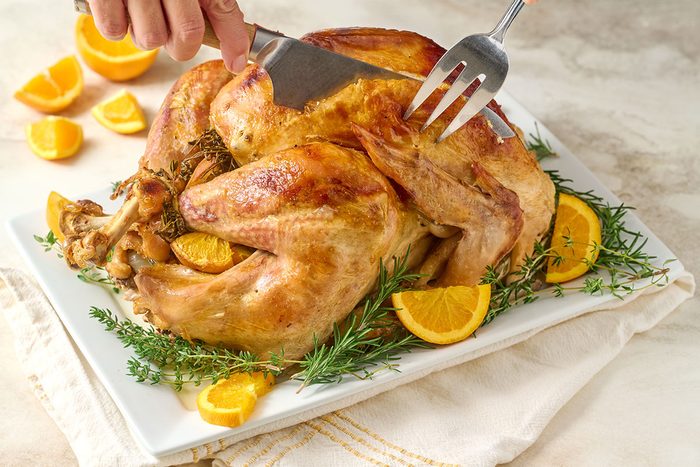 Close-up horizontal shot of the Taste of Home Orange Turkey, getting carved and highlighting the golden, crispy skin and fresh herb garnish.