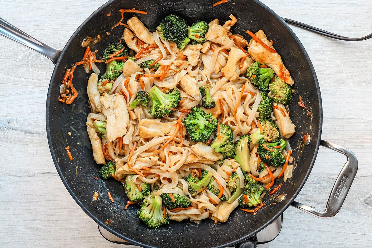 Combining the stir-fried vegetables with the sauce, cooked chicken and rice noodles for peanut chicken stir-fry.