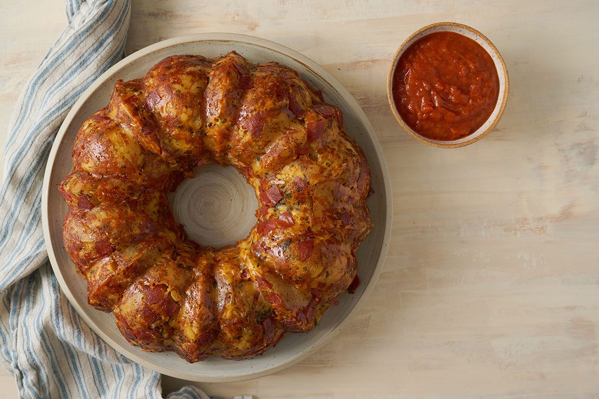 Overhead hero shot of the finished Taste of Home Pull Apart Pizza bread, golden brown and served warm on a plate with a side of marinara for dipping.