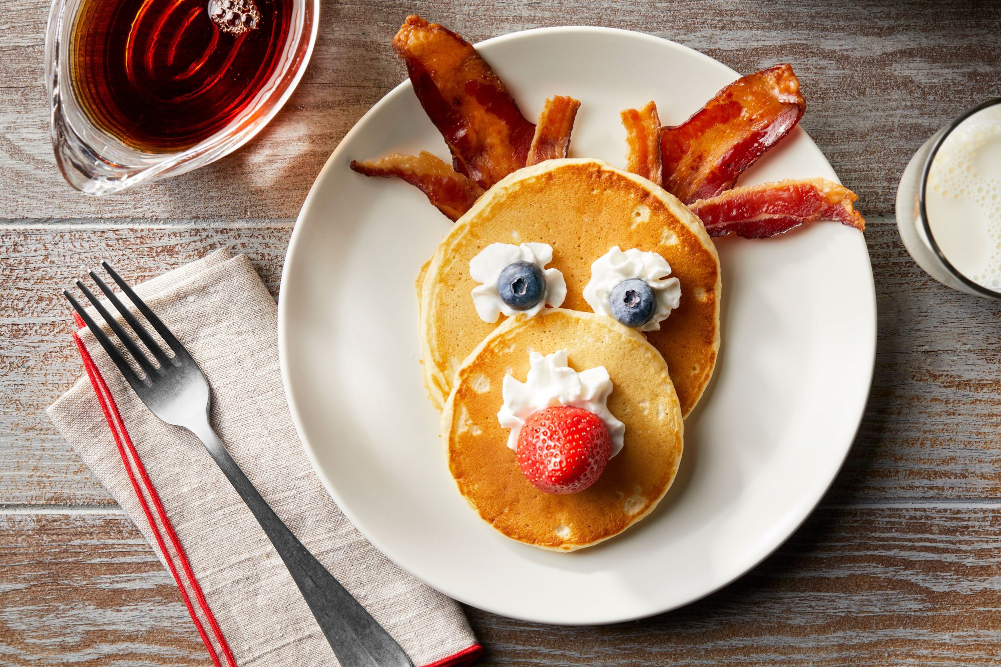 Assemble reindeer pancakes with whipped cream, blueberries, strawberries, and beacon
