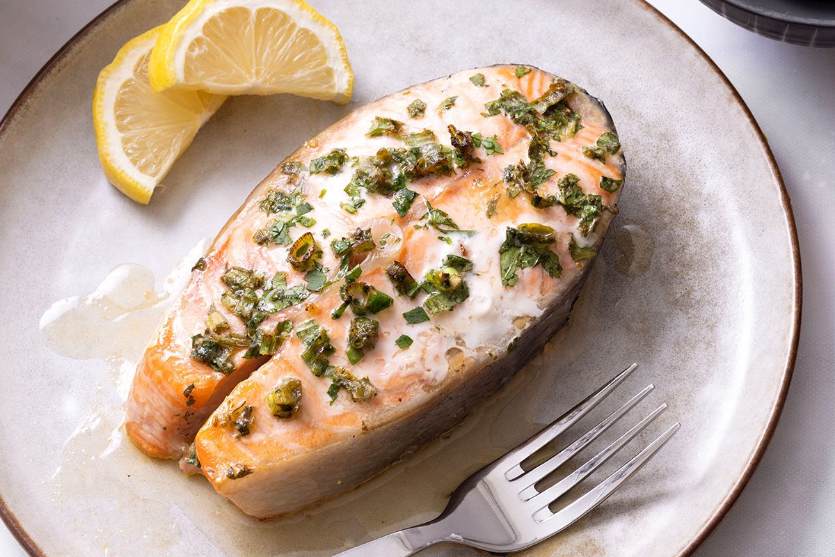 One Salmon Steak with lemon slices on a plate and fork for Taste of Home