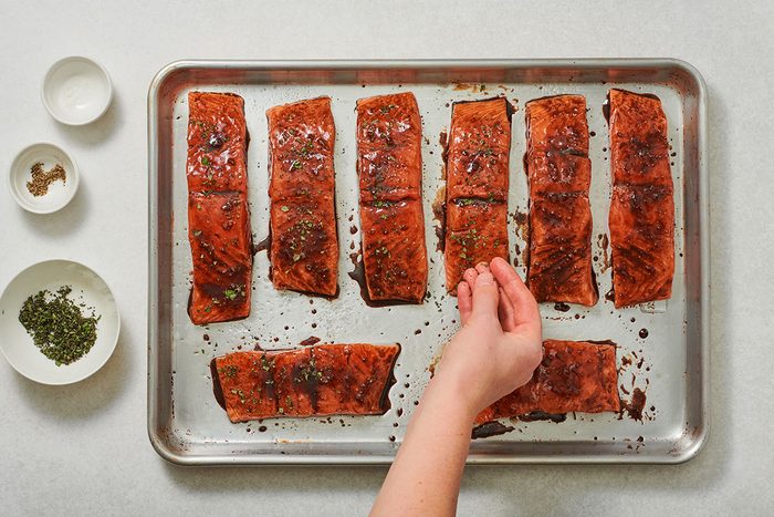 Salmon fillets coated in balsamic glaze and sprinkled with fresh oregano on a baking sheet