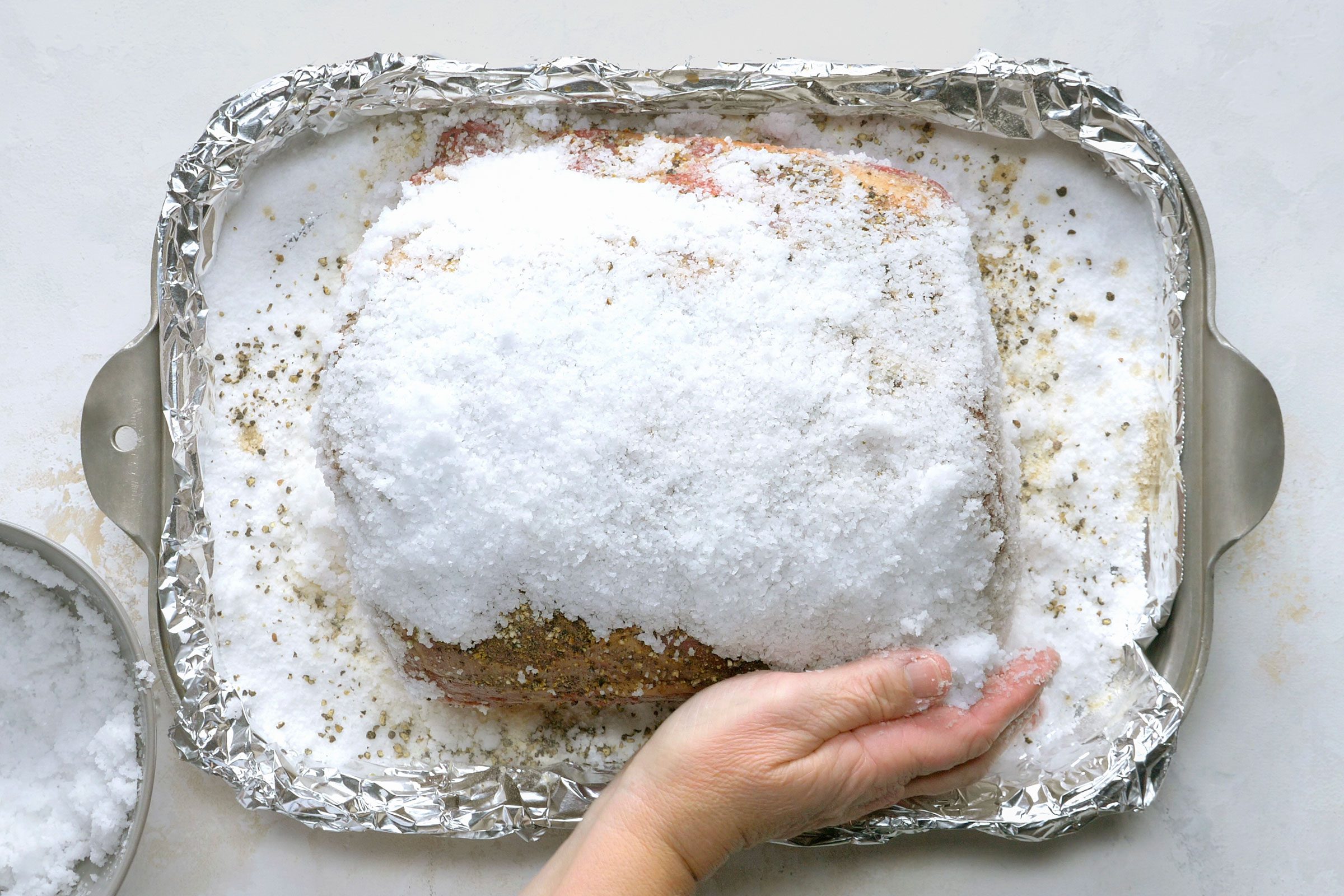 Prime roast rib covered in seasonings and kosher salt on a shallow pan.