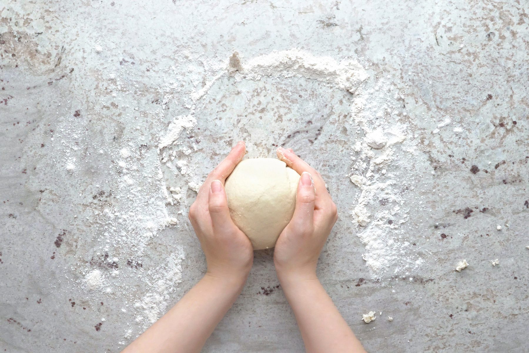 Hands kneading dough on a marble surface for scallion pancakes.