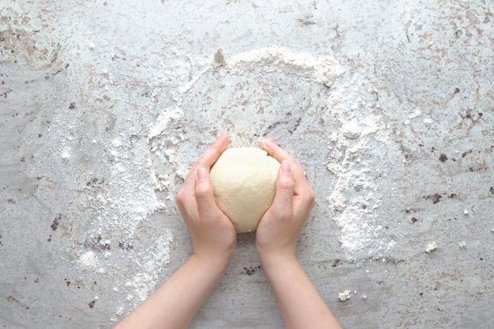Hands kneading dough on a marble surface for scallion pancakes.