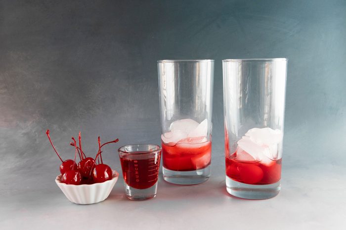 Drop two maraschino cherries into the bottom of the glass, then fill it halfway with ice cubes and pour 1 ounce of grenadine syrup