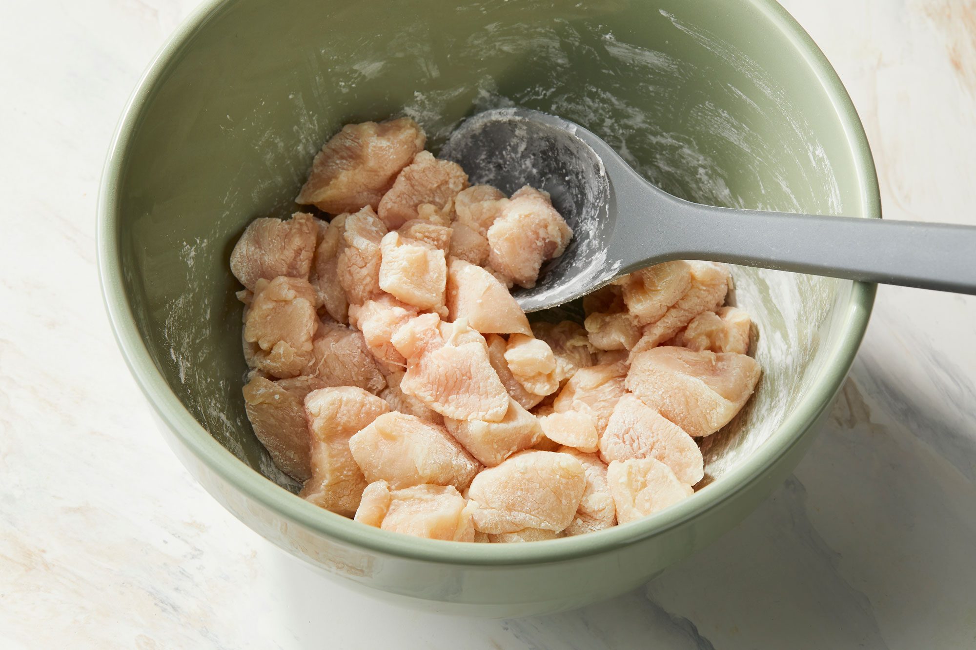 A large bowl tossing chicken with cornstarch, a gray spatula is resting in the bowl