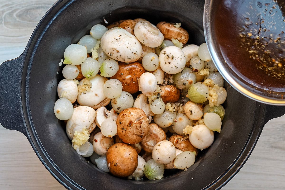 The beef and red wine broth is poured over the mushrooms and onions in the slow cooker.