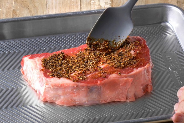 seasoning is being rubbed over steak on a tray