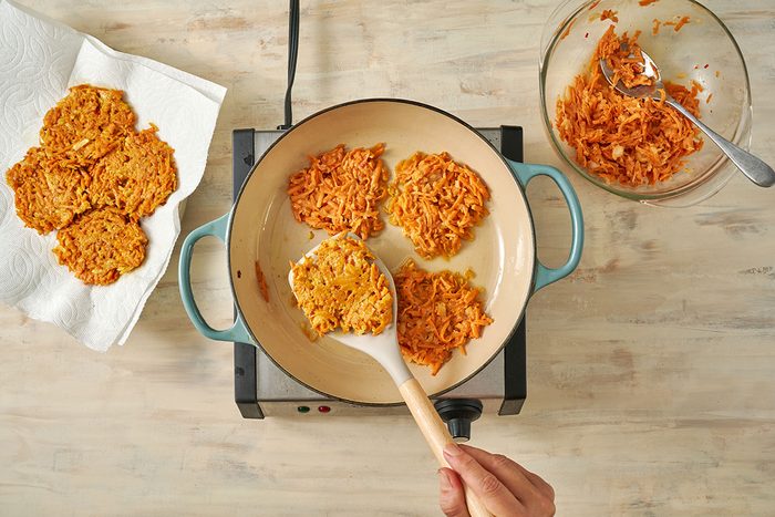 Overhead view of the sweet potato mixture being dropped by 1/4 cupfuls into a skillet with coconut oil, frying until golden brown for the Taste of Home Sweet Potato Fritters recipe.