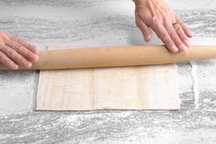 Rolling pastry dough sheet using a rolling pin on a floured surface
