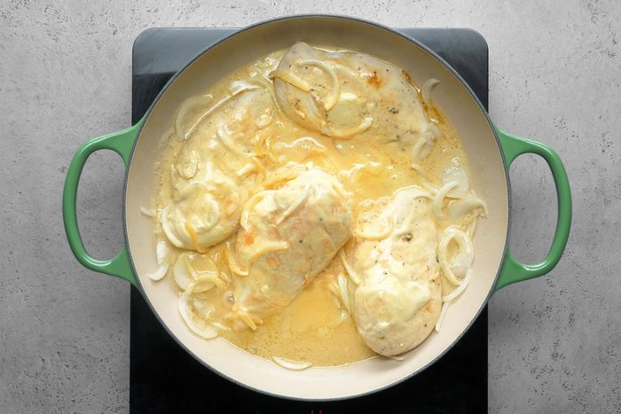 Chicken breasts cooking in a large skillet with onions and cream mixture in it