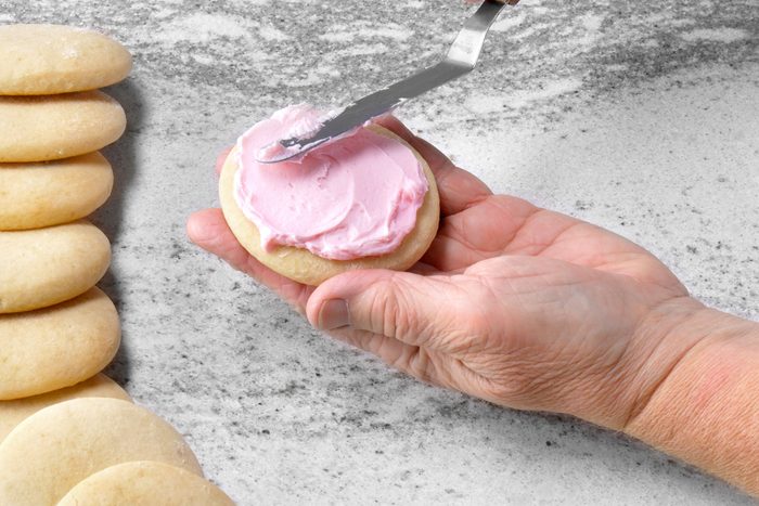 Spreading pink colored cookie frosting on baked cookie with a spatula