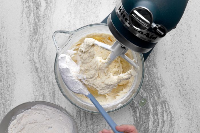 Flour added using a serving spoon to the butter, sugar and cream mixture in a large bowl