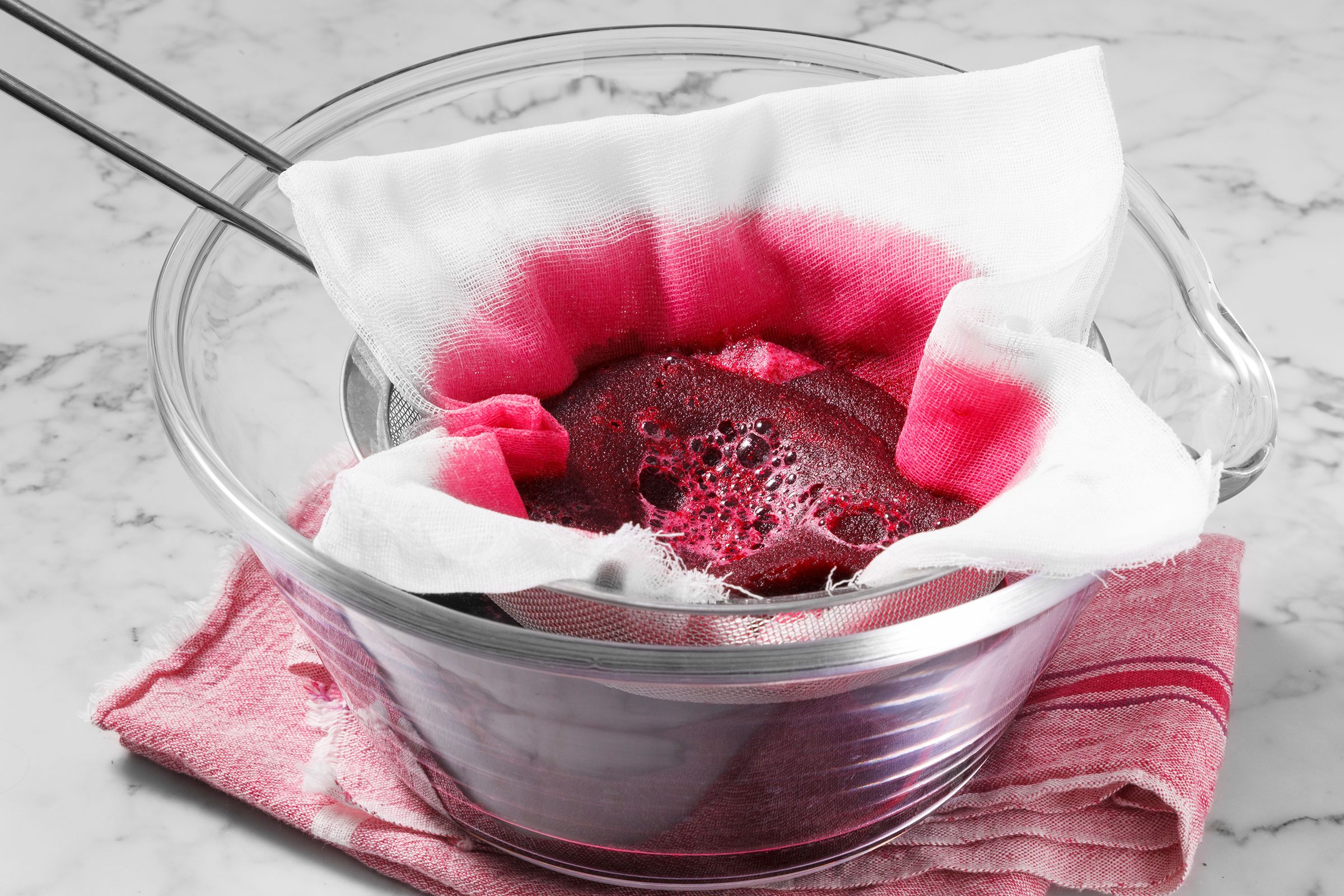 Straining blended beet and water mixture through a colander with lined cheesecloth