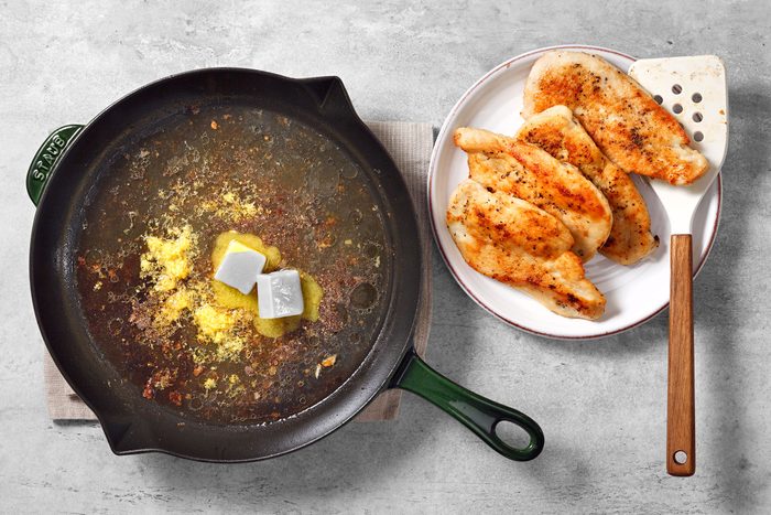 Butter, chicken broth, lemon zest and seasoning in a large skillet with golden brown chicken breasts on the side