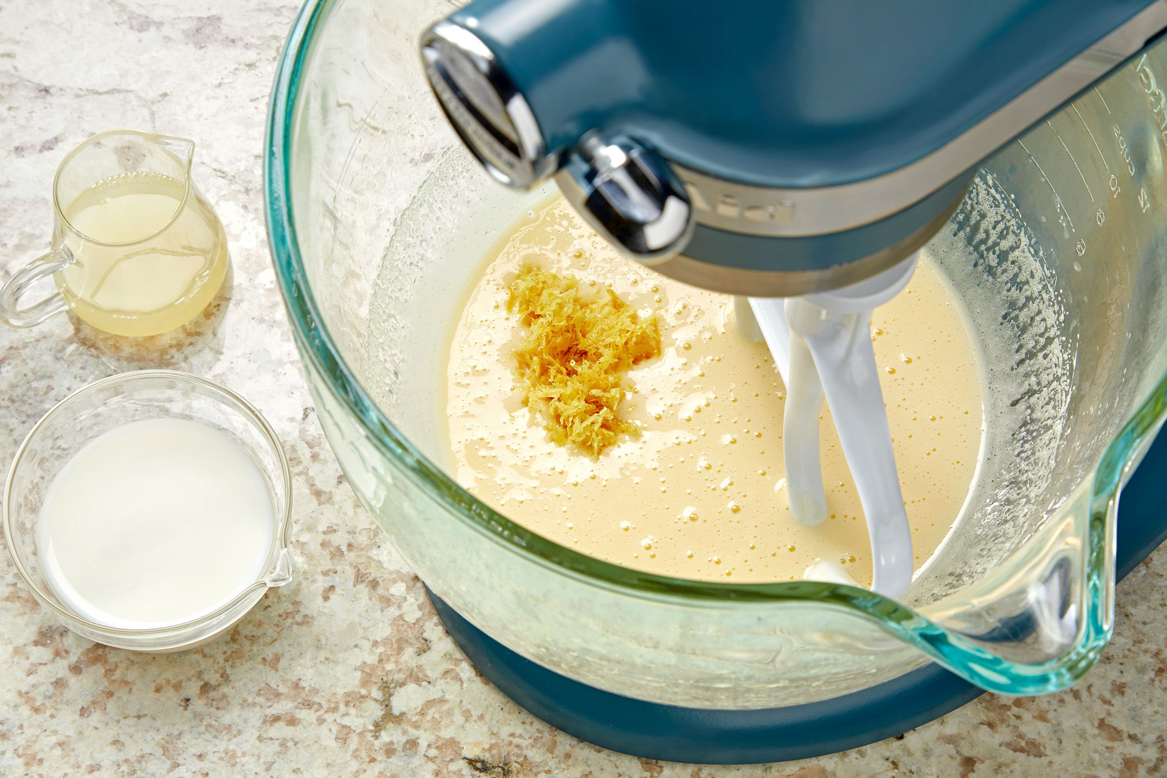 Adding lemon zest to the beaten eggs and sugar mixture in a glass bowl