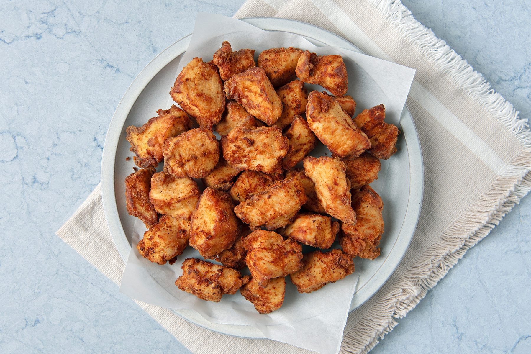 A plate of fried chicken pieces on a light-colored napkin and marble surface.
