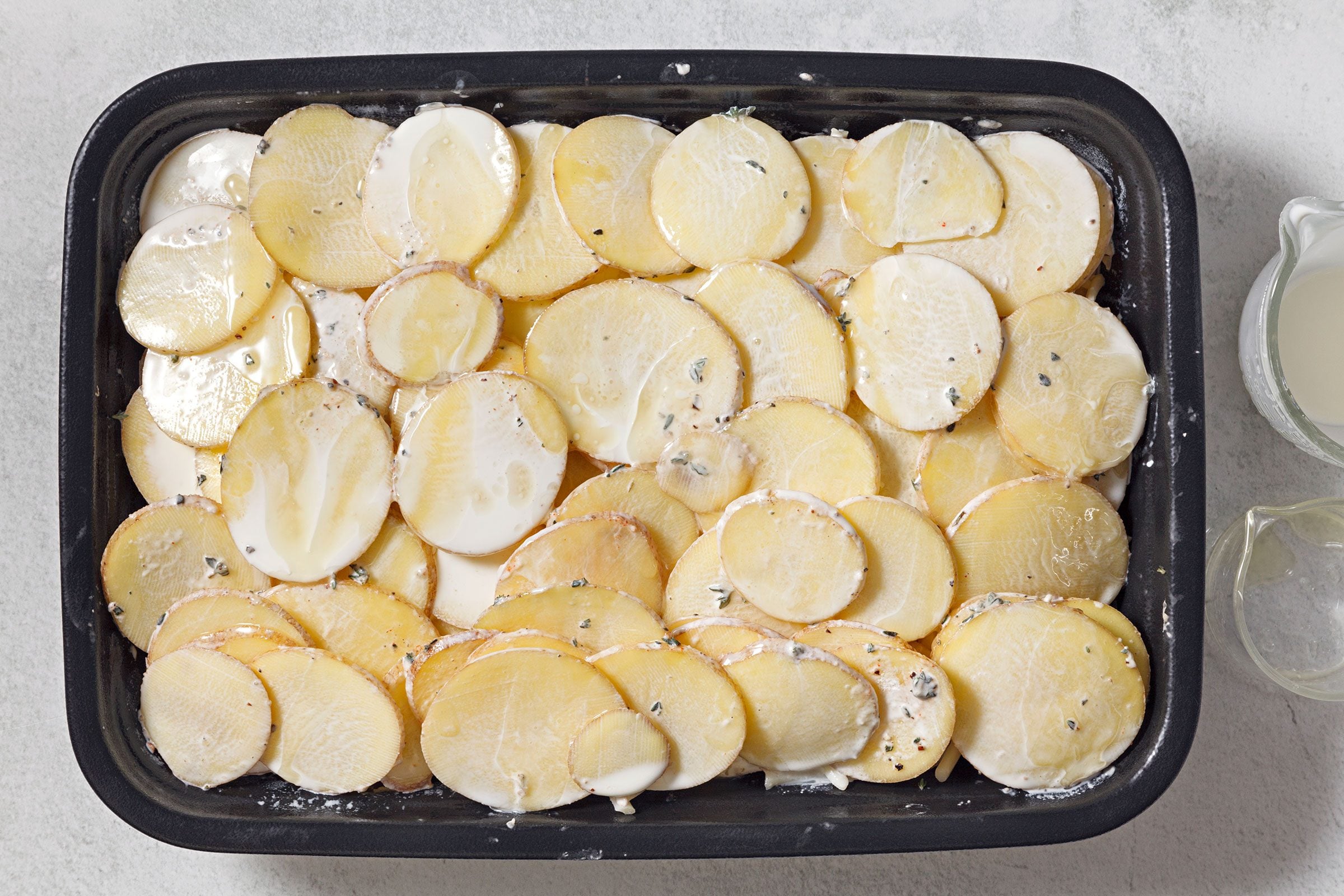 Seasoned potato slices spread on greased baking dish 