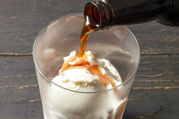 Pouring root beer over vanilla ice cream in a glass