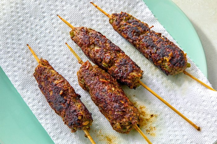 overhead shot of four kebabs on a white paper towel; the kebabs are on skewers, and they are resting on a light blue plate