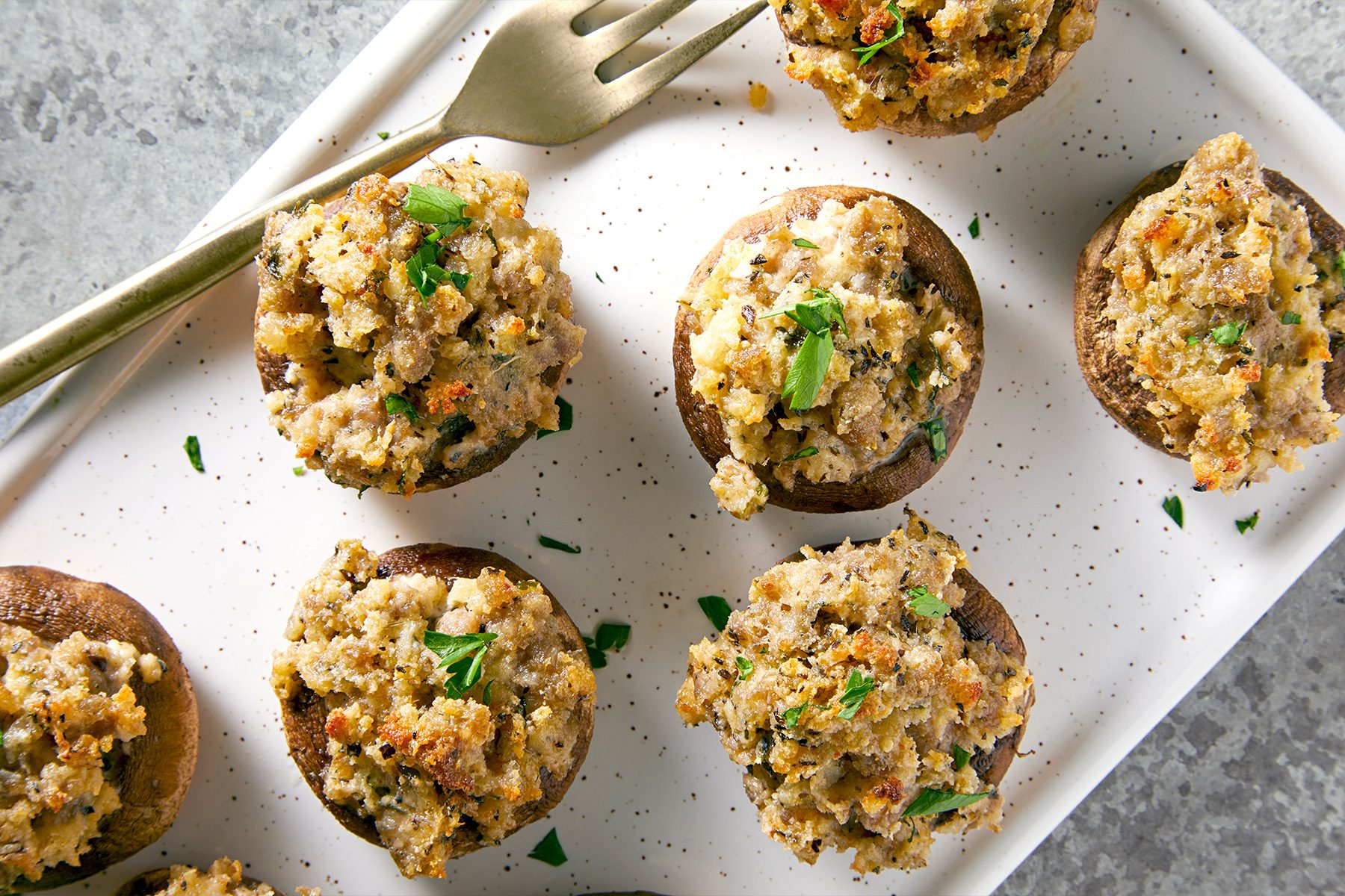 A white platter filled with stuffed mushrooms, accompanied by a fork resting beside them.