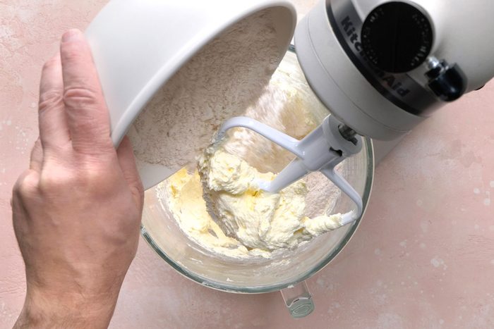Adding dry ingredients for cookies to the creamed butter mixture in a bowl