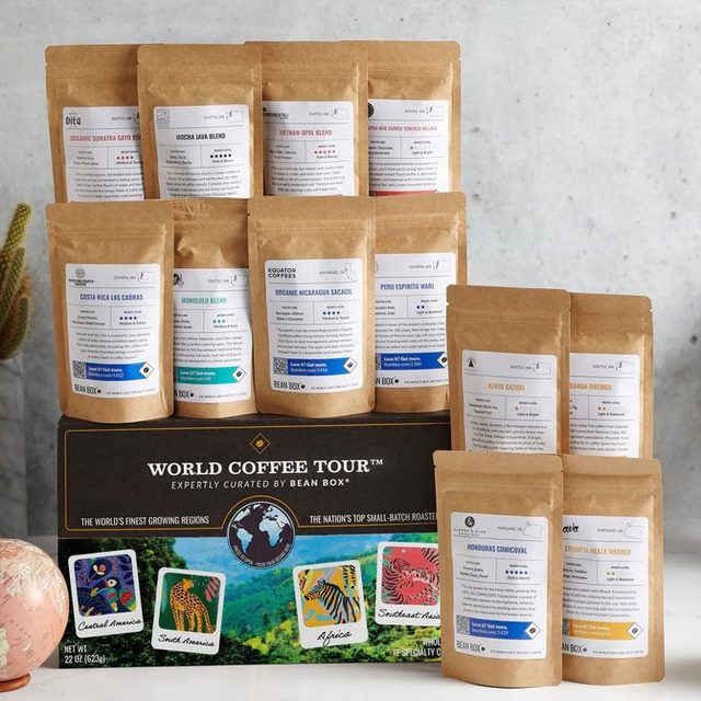 12 bags of the BeanBox World Tour Coffee Set, pictured with a plant, globe, and mug on a plain background