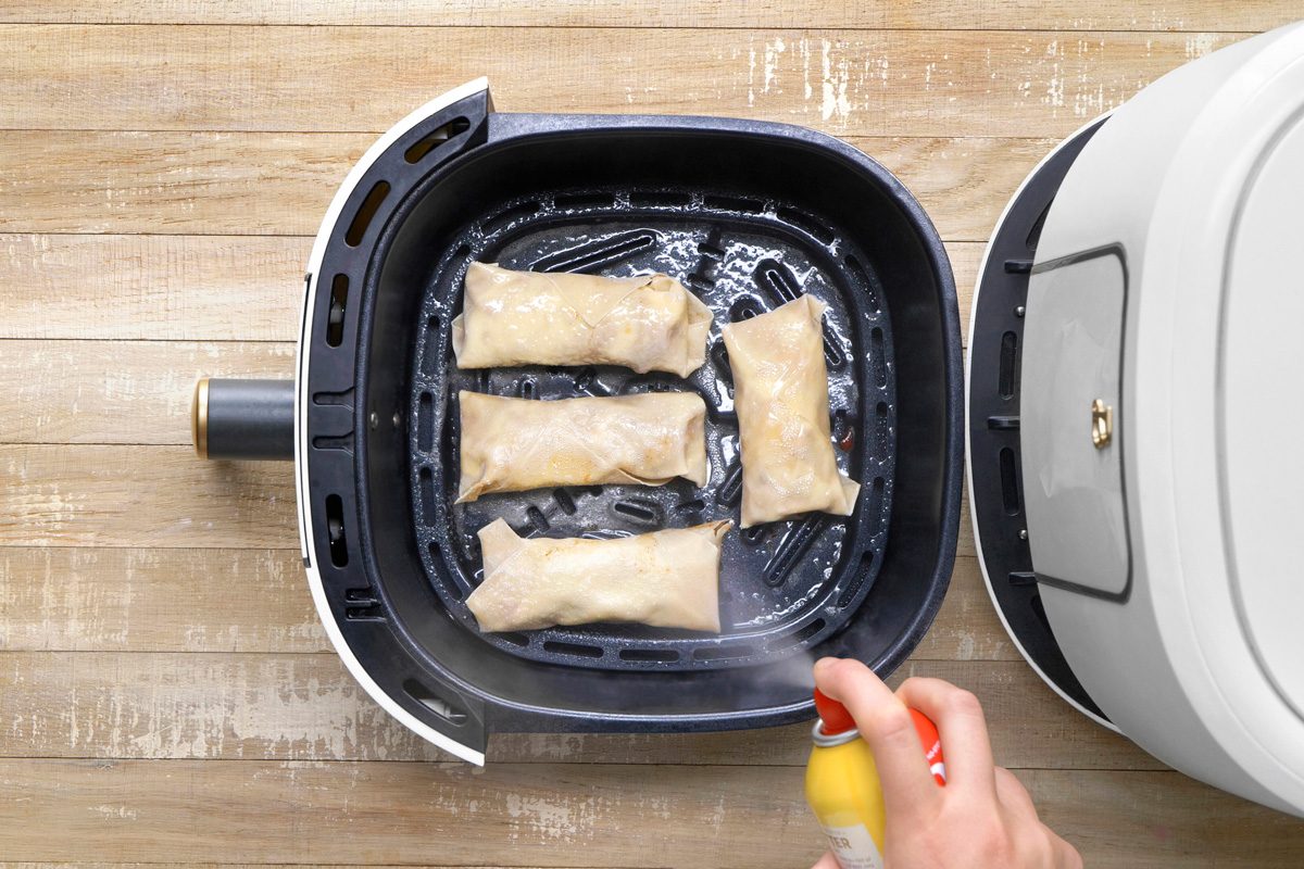 egg rolls being fried in a single layer on the greased tray in the air fryer basket