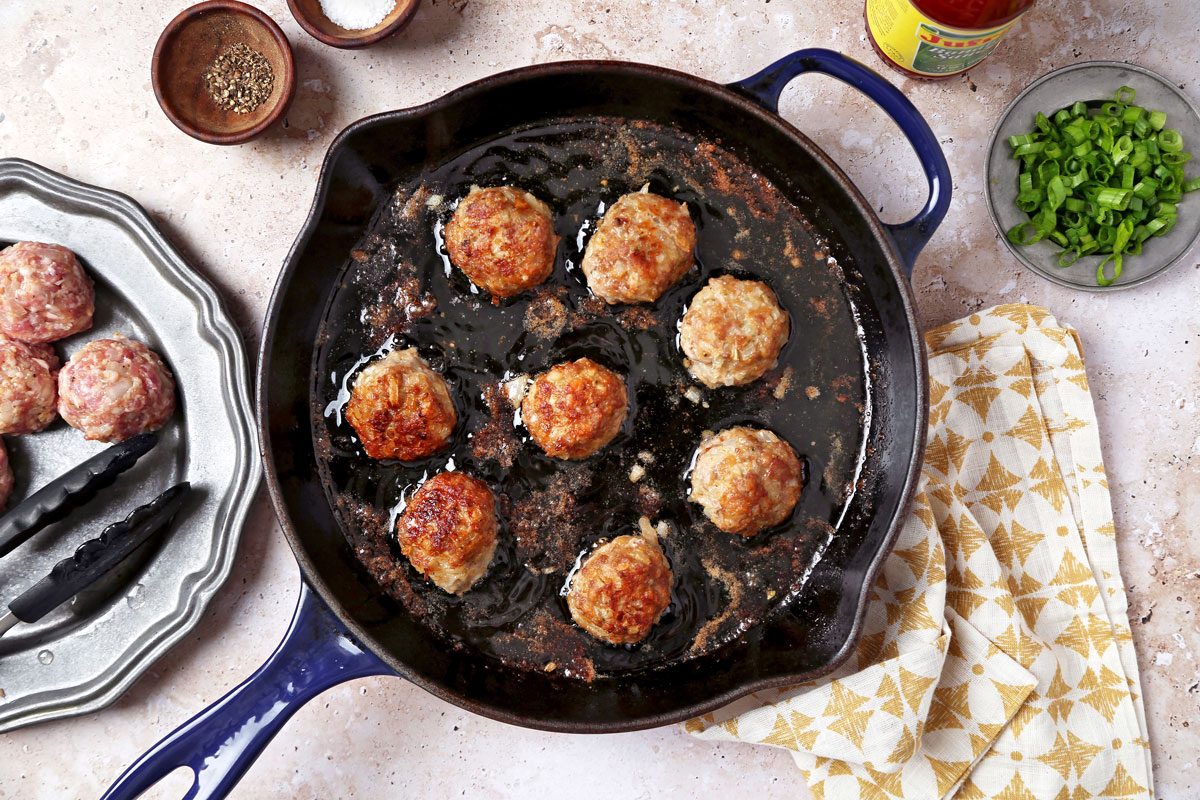 Meatballs fried in a skillet with oil.