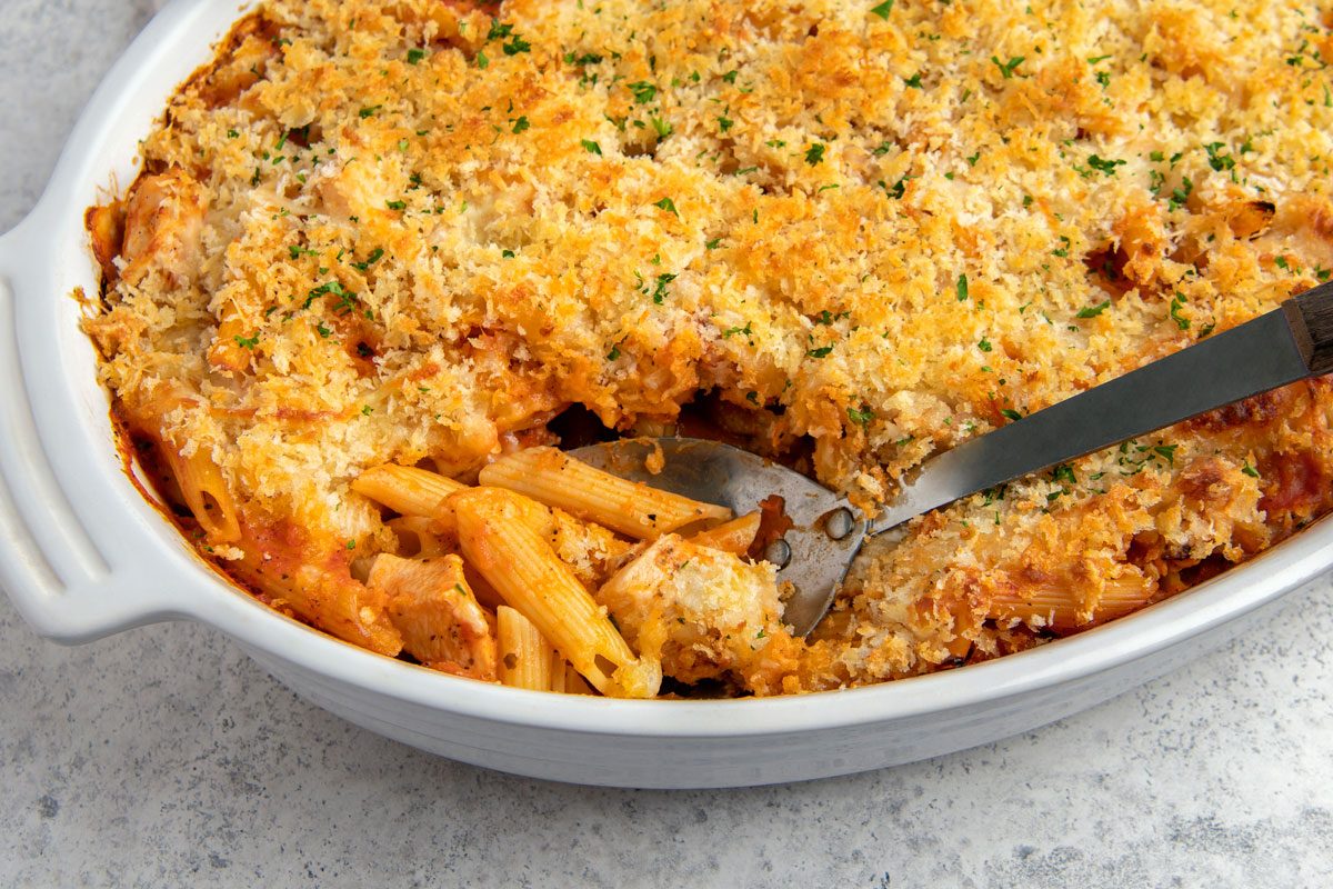 Close shot of Chicken Parmesan Casserole; in a baking pan; serving spoon; napkin; marble surface;
